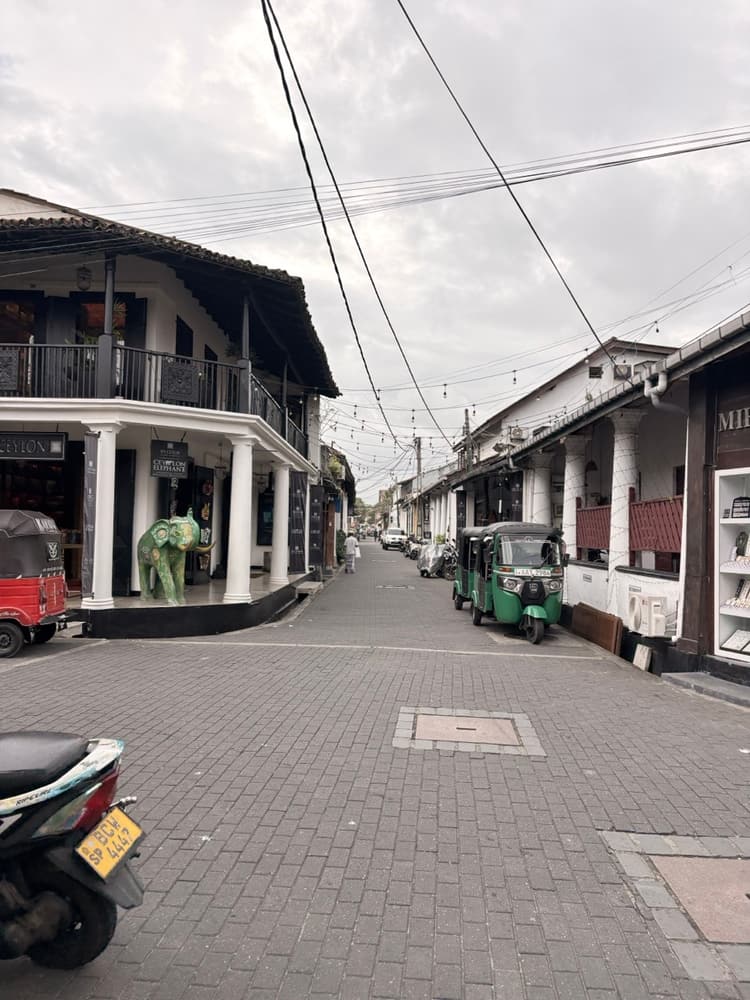 Pillared two-storey colonial shopfronts and parked tuk-tuks along a quiet paved street inside Galle Fort, Sri Lanka