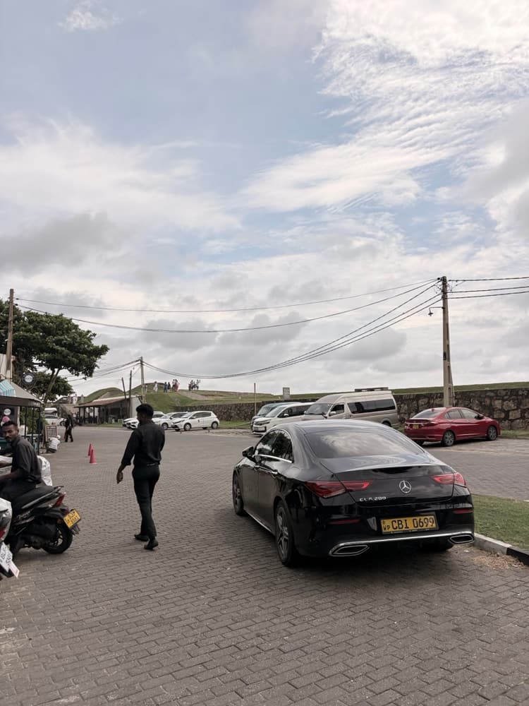Cars and vans parked beside the grassy Galle Fort ramparts, a convenient taxi drop-off and pickup point for visitors to the old town