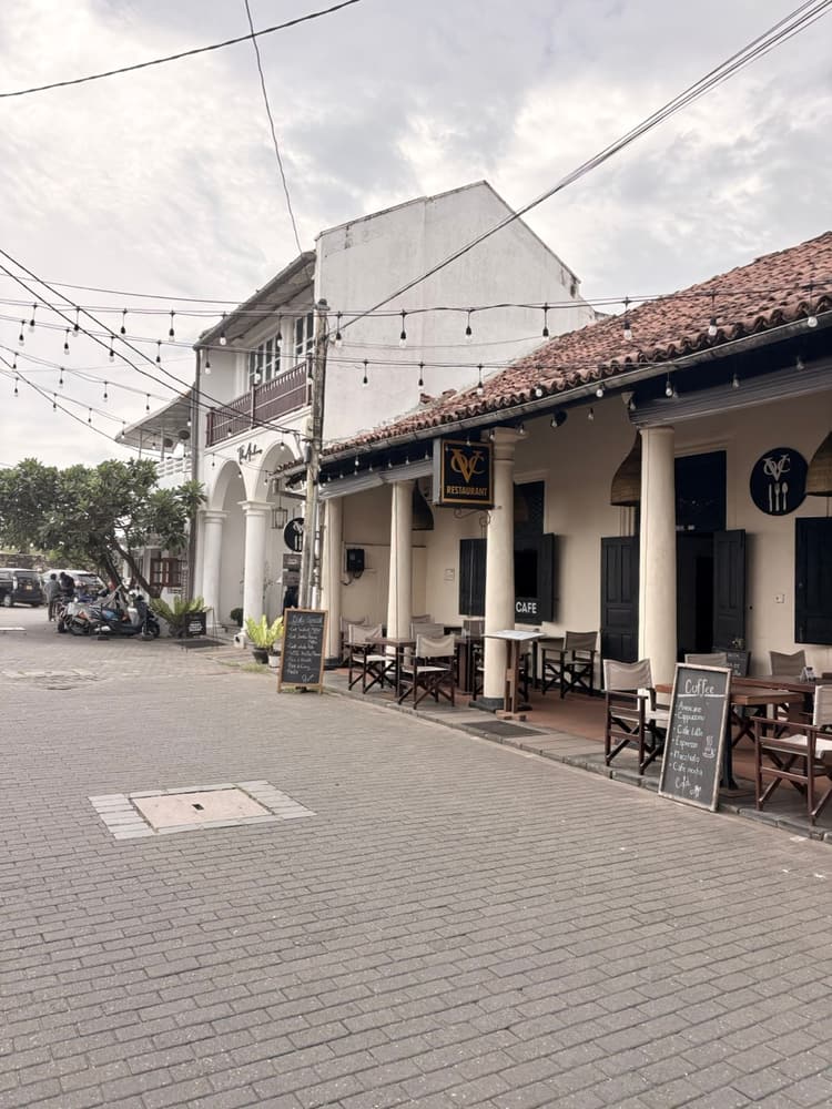 Restaurant and café with outdoor tables under a pillared tiled-roof verandah on a wide street in Galle Fort
