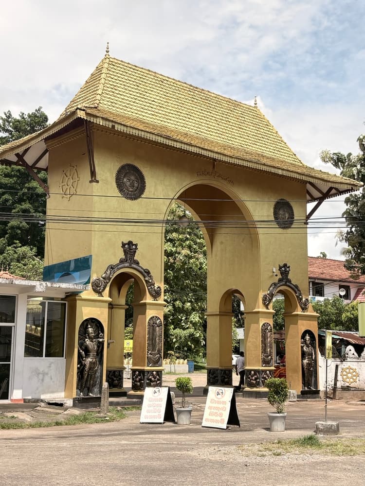 Ornate yellow temple gateway with tiled roof, carved guardian figures and a sun emblem above the arch
