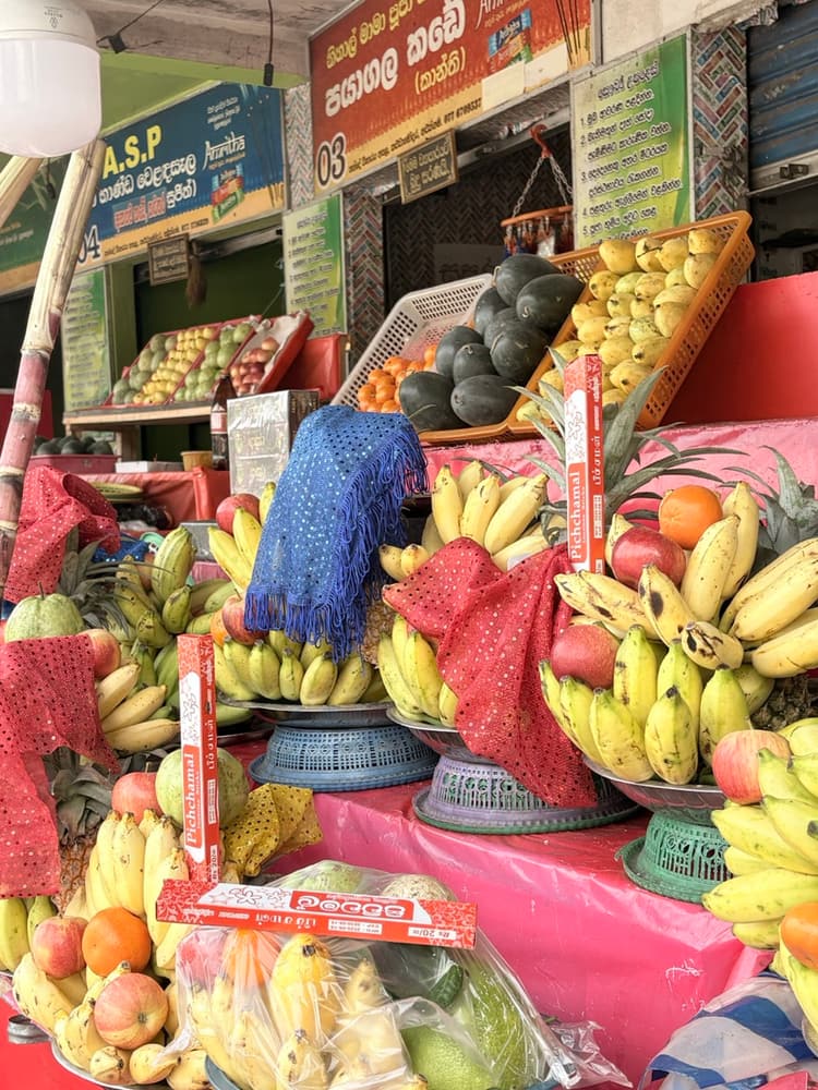Stall stacked with bananas, pineapples and pomegranates arranged on trays with red cloth