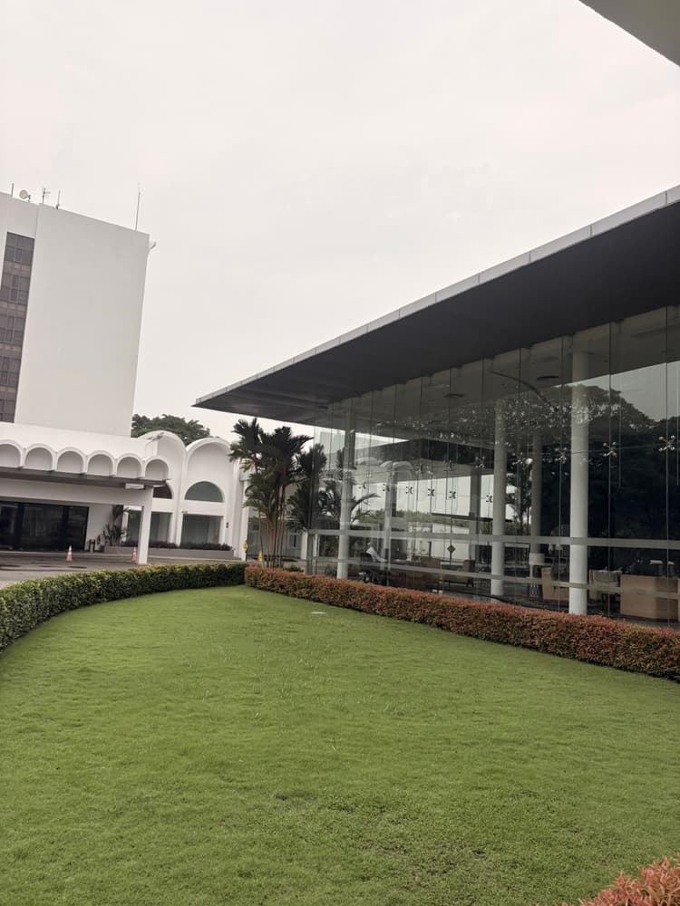 White arched hotel wing beside the glass lobby pavilion and a lawn at Vivanta Colombo Airport Garden